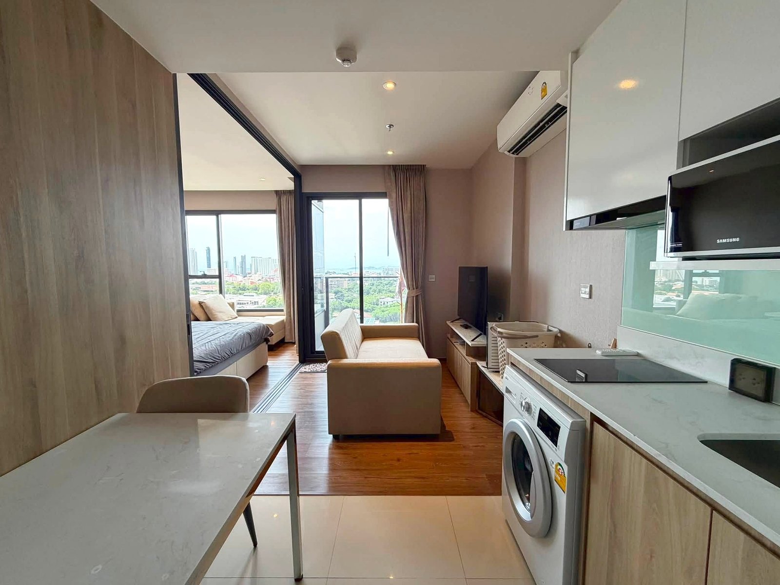 Once_Pattaya_Rent_Rdl366_3 Open-plan studio apartment with kitchen on the right, living area in the center, bed alcove to the left, and large city-view windows at the back.