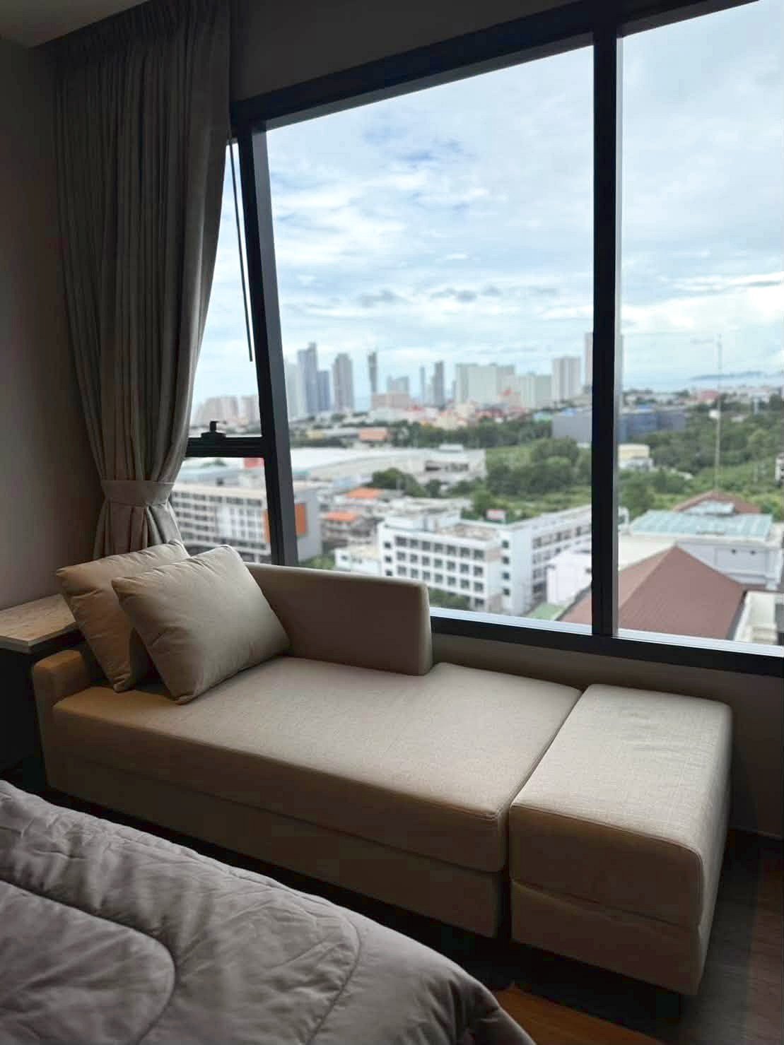 Once_Pattaya_Rent_Rdl366_4 Beige window seat with cushions beside a large floor-to-ceiling window showing a city skyline outside.