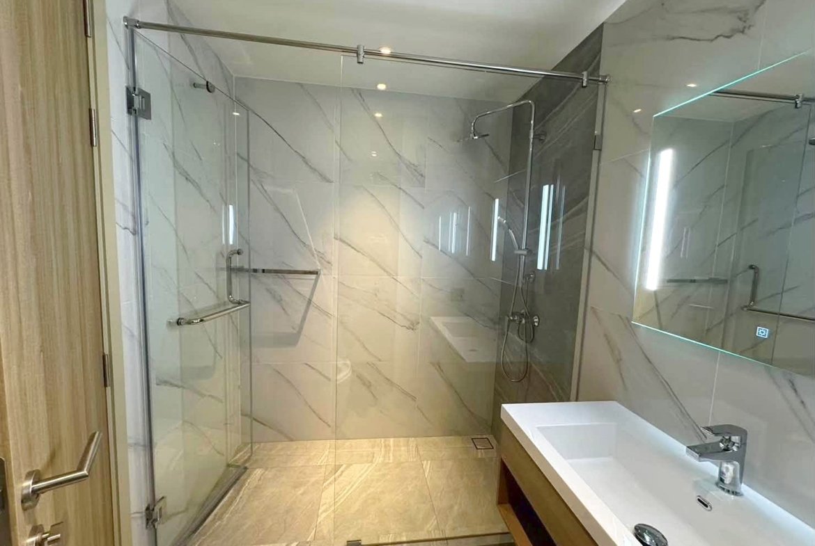 Modern bathroom with glass-walled shower, marble walls, and a white rectangular sink