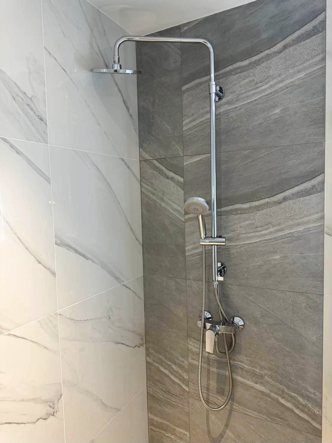 Once_Pattaya_Rent_Rdl366_7 Modern shower with a curved chrome rain shower arm, a ceiling-style head, and a handheld wand on a vertical bar against gray-veined tiles.