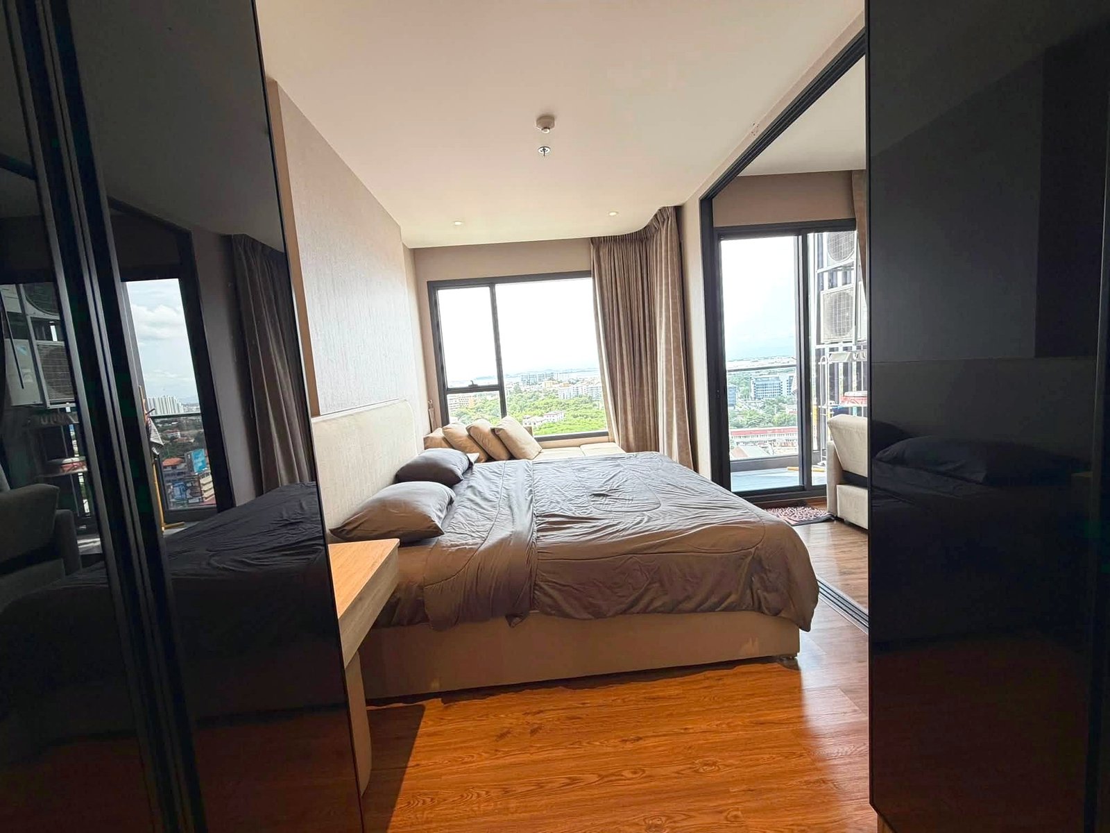 Once_Pattaya_Rent_Rdl366_8 Hotel bedroom with a large bed, beige bedding, and floor-to-ceiling windows showing a city skyline.