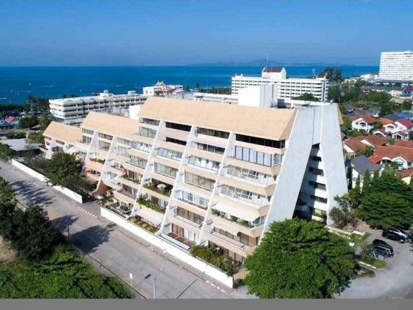 Aerial view of a beige, pyramid-shaped seaside apartment building with balconies and the ocean beyond.