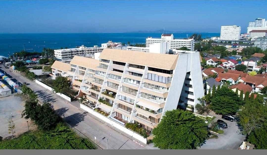 Aerial view of a beige, pyramid-shaped seaside apartment building with balconies and the ocean beyond.