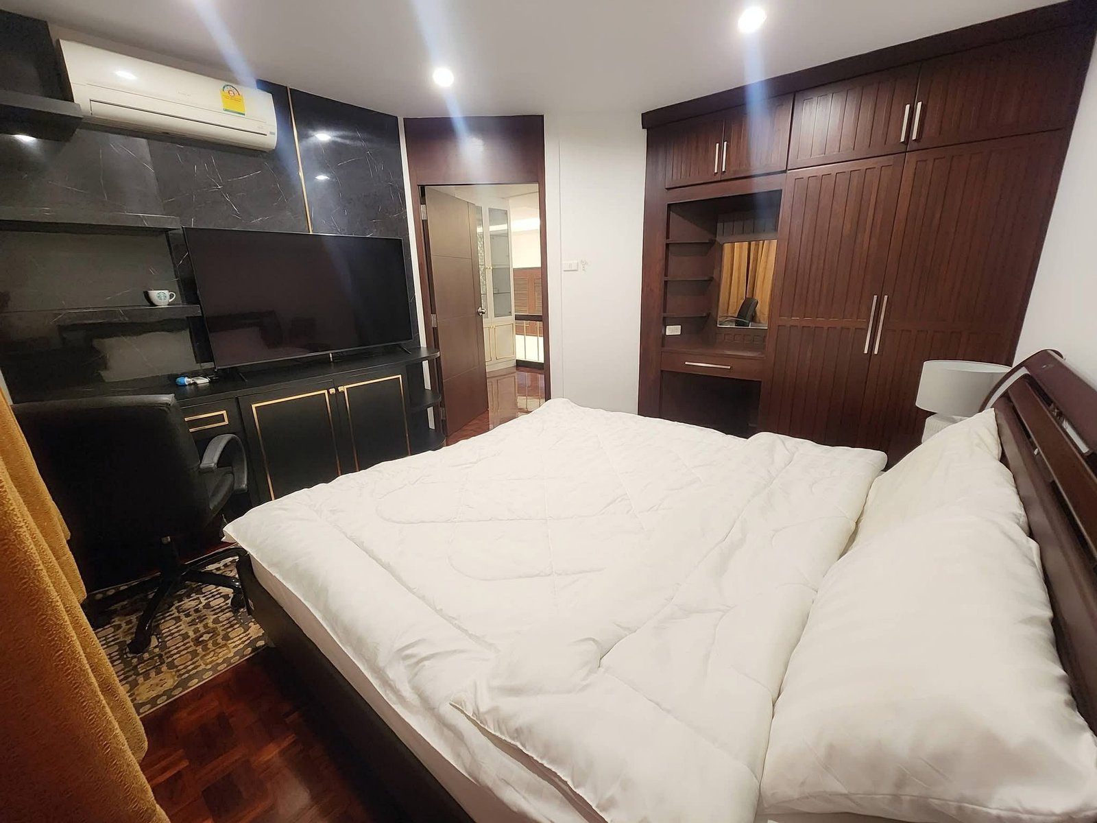 PANCHALEA_RESIDENCE_Jomtien_Rdl290_10 Bedroom with white quilted bed, dark wood wardrobes, and a flat-screen TV on a black marble wall.