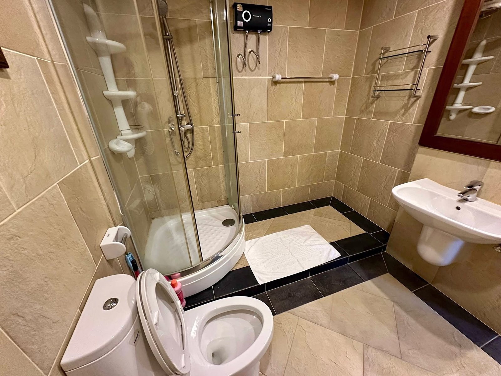 PANCHALEA_RESIDENCE_Jomtien_Rdl290_11 Small tiled bathroom with a curved glass shower enclosure, open toilet seat, sink, and wall mirror across beige walls and floor.