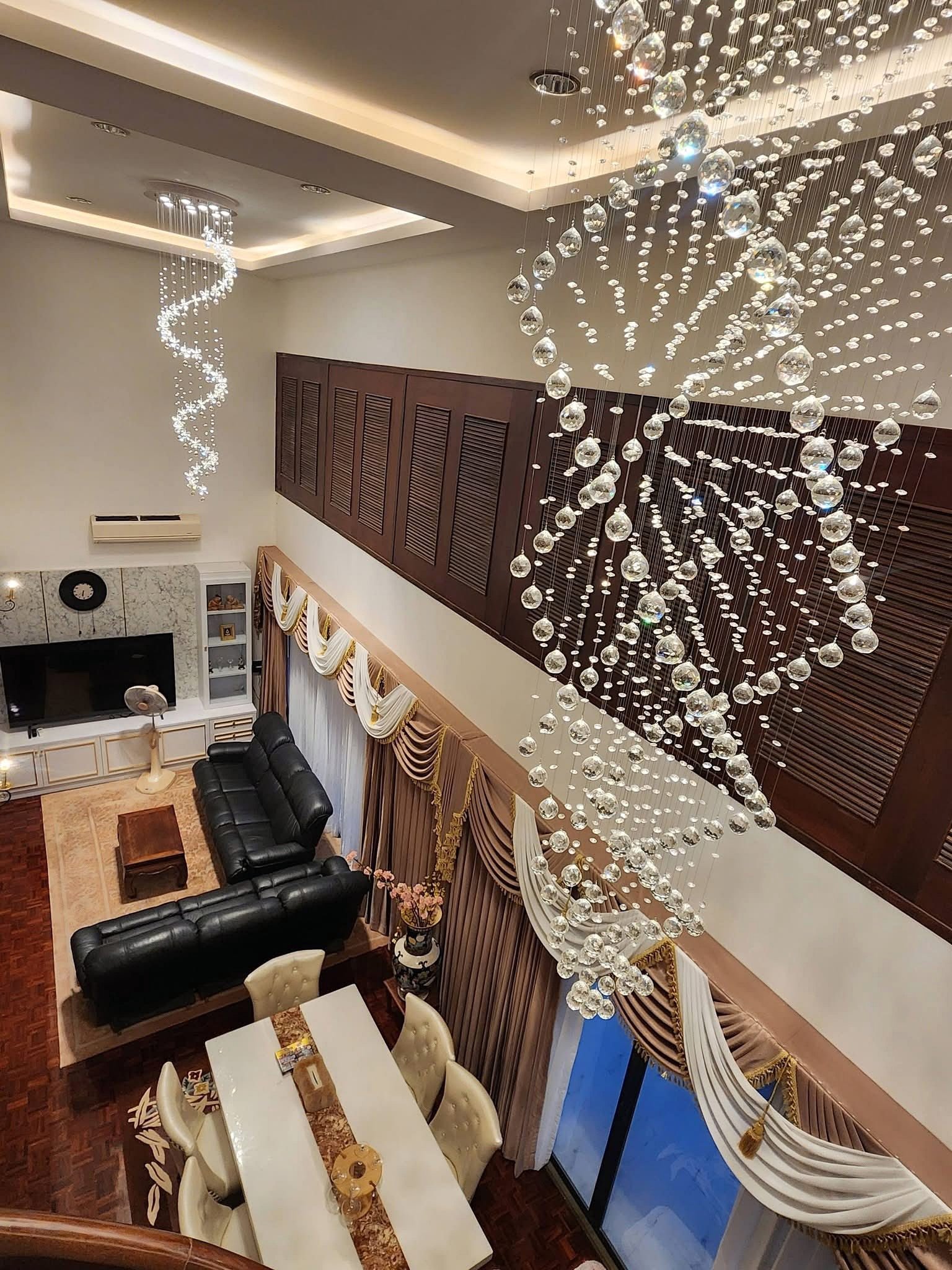PANCHALEA_RESIDENCE_Jomtien_Rdl290_17 Luxurious living room with cascading crystal chandeliers, dark wood cabinets, and a marble fireplace surrounding a white dining table set.