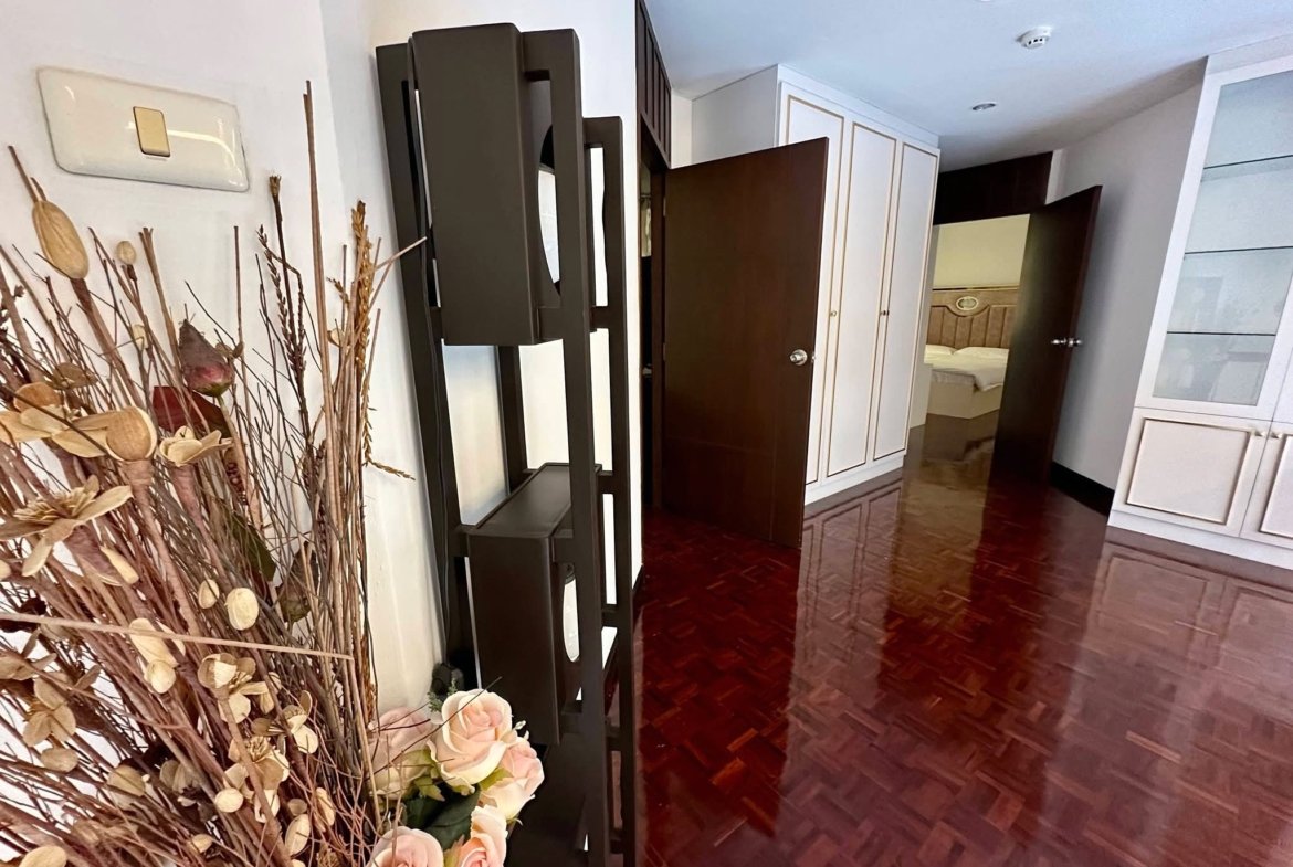 Hallway view with dark wood furniture, white cabinets, and a bouquet of dried branches and pale pink roses in the foreground.