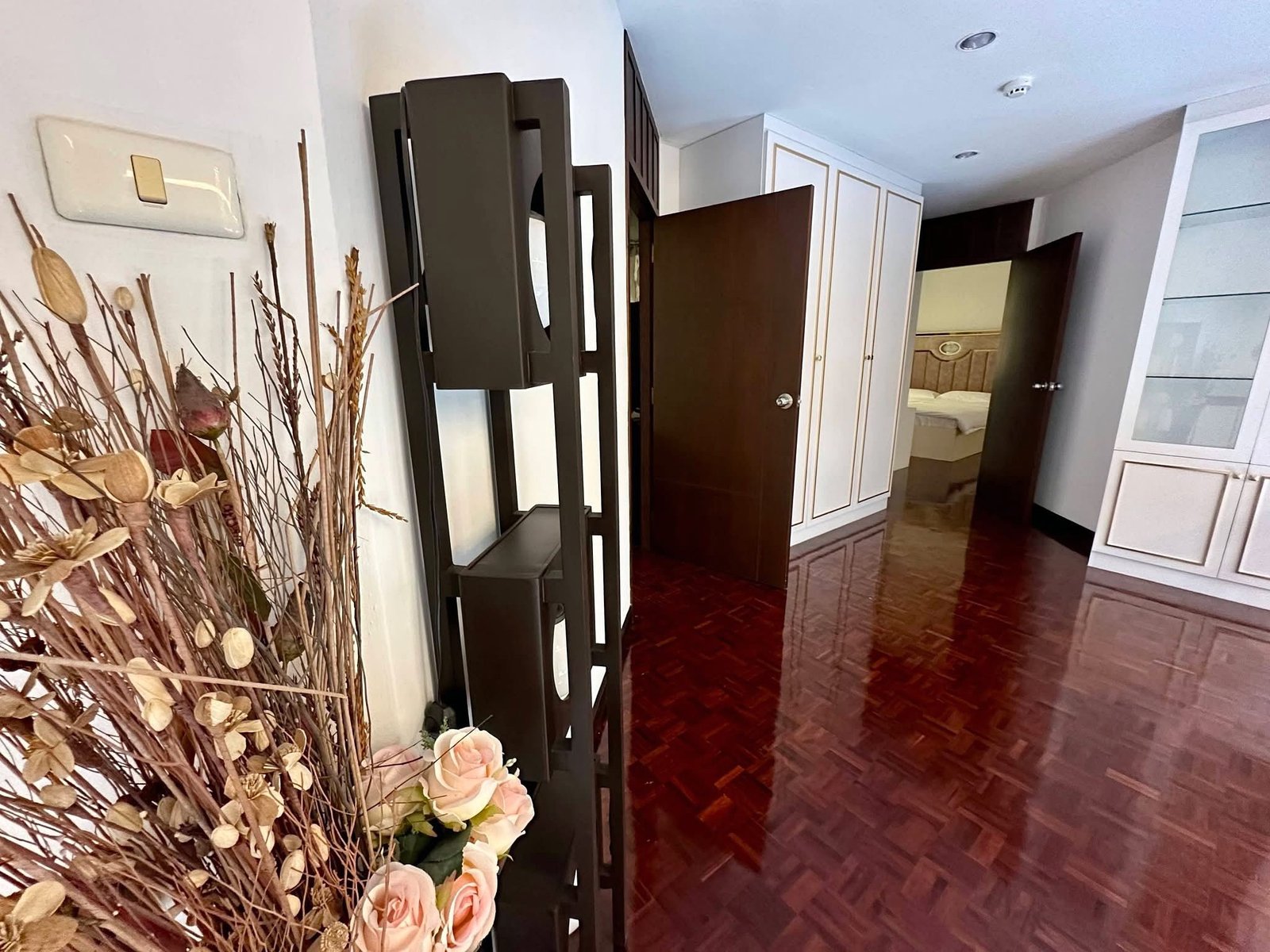 PANCHALEA_RESIDENCE_Jomtien_Rdl290_19 Hallway view with dark wood furniture, white cabinets, and a bouquet of dried branches and pale pink roses in the foreground.