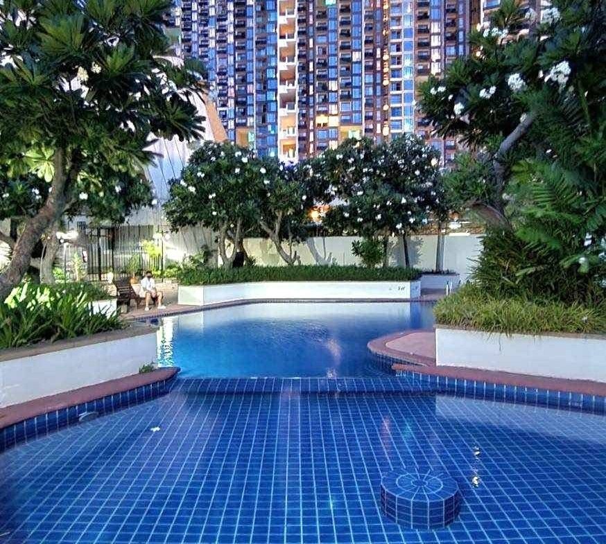 Curved blue-tiled pool in a courtyard with trees and a tall modern apartment building in the background.