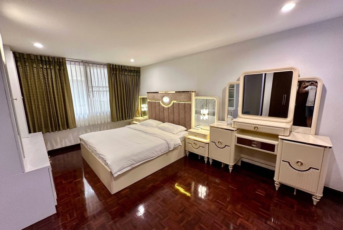 Bright bedroom with white ornate furniture, a large bed, mirrored dresser, and dark wooden floor.