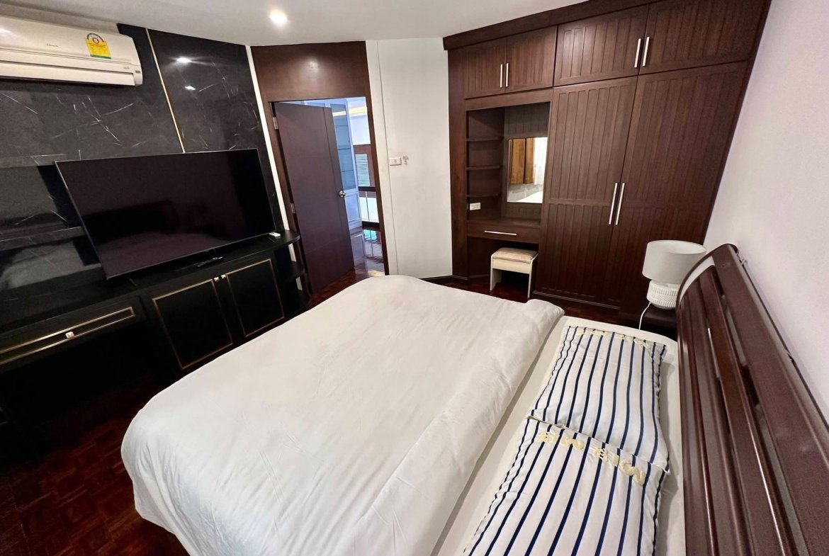 Twin beds with white duvets and navy striped pillows in a wood-furnished hotel-style bedroom with a flat-screen TV and dark wardrobe.