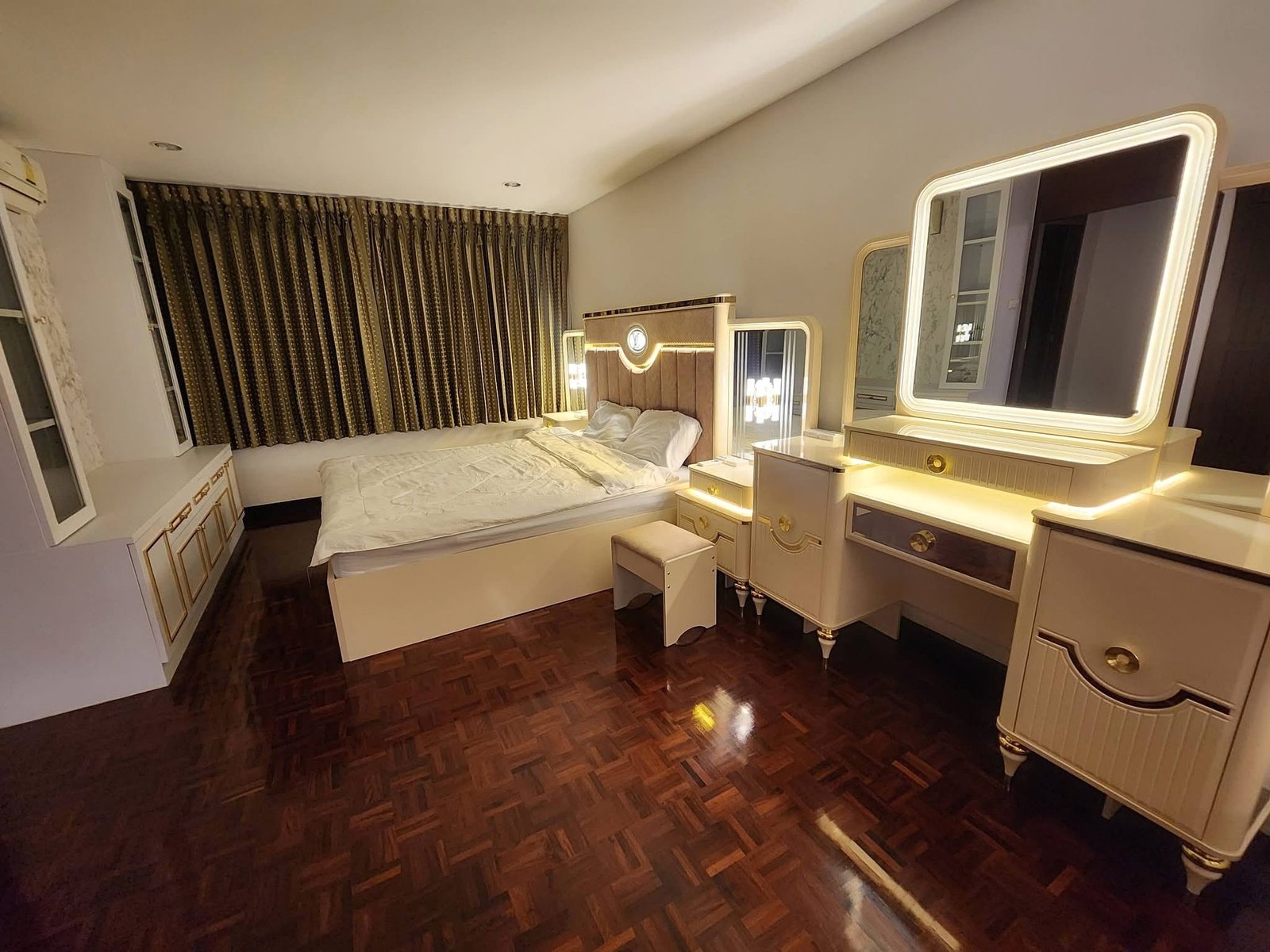 PANCHALEA_RESIDENCE_Jomtien_Rdl290_8 Hotel bedroom with a tufted headboard, white vanity and illuminated mirror, and long patterned drapes along a large window.