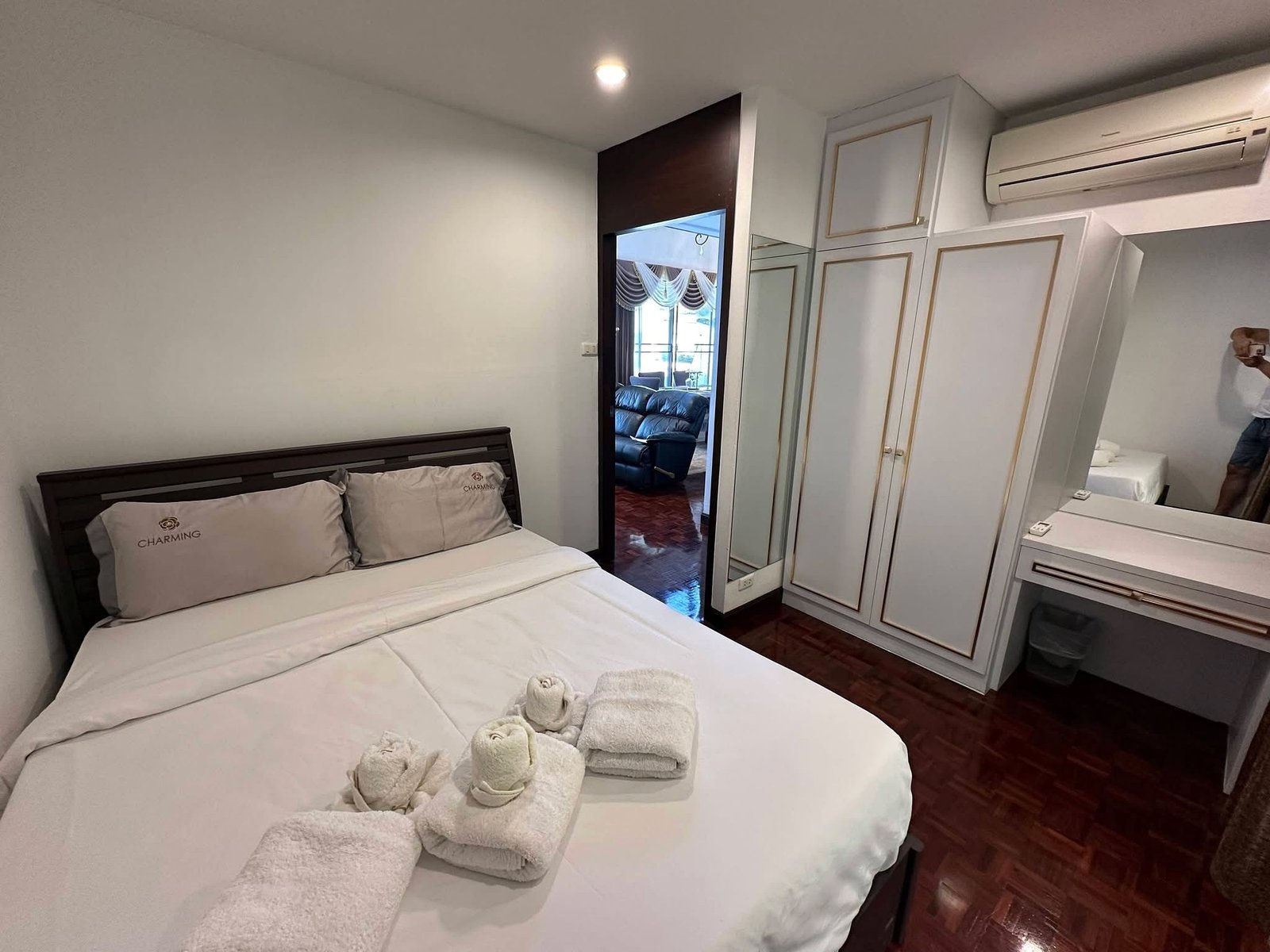 PANCHALEA_RESIDENCE_Jomtien_Rdl290_9 Hotel-style bedroom with a white bed, two gray pillows marked 'CHARMING', and rolled towels at the foot of the bed, plus a dark wood headboard and mirrored wardrobe doors.