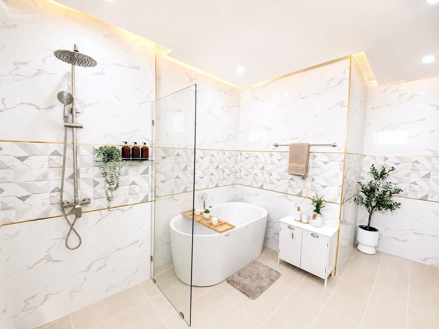Modern spa-style bathroom with a freestanding white tub, glass divider, and a rainfall shower on the left; geometric tile accent and marble walls brighten the space.