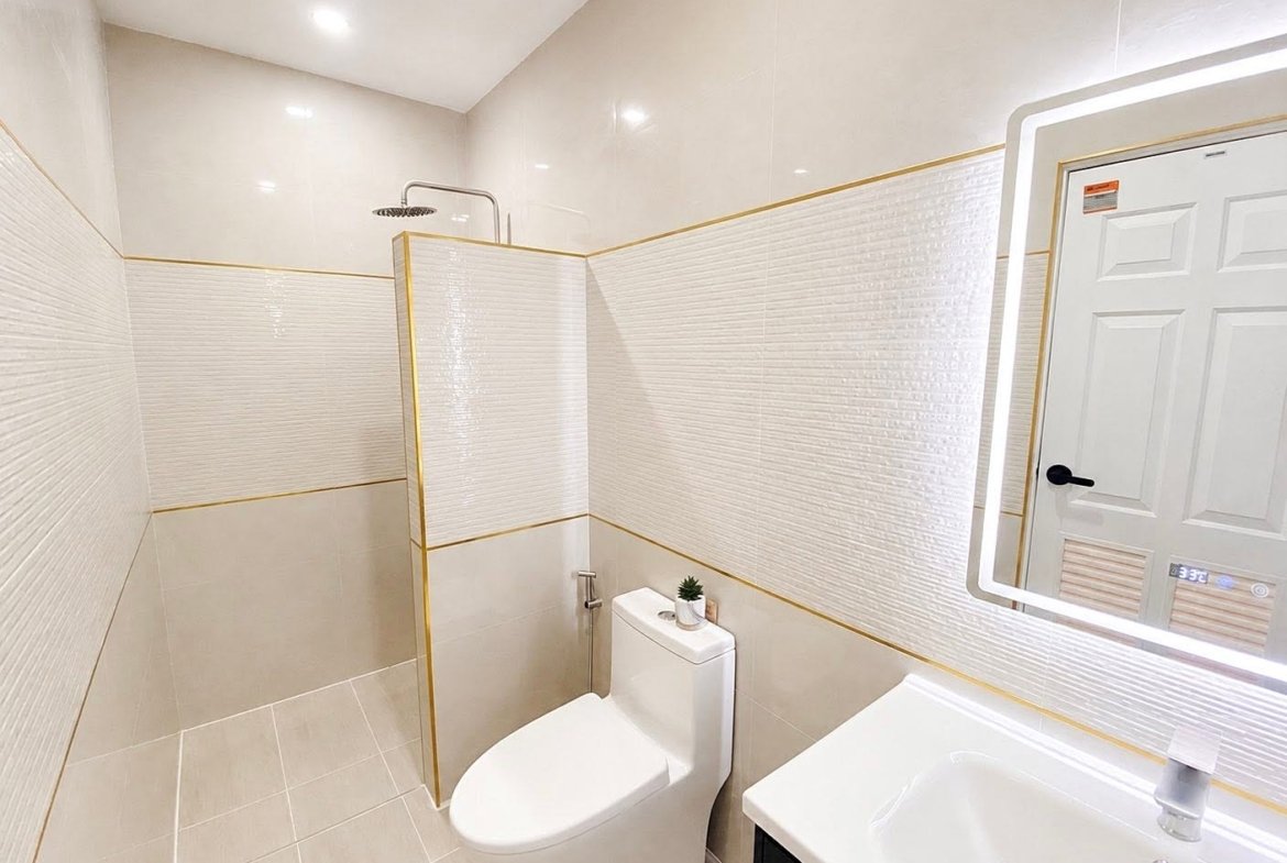 Small modern bathroom with a walk-in shower, white toilet, and sink with a backlit mirror on the wall.