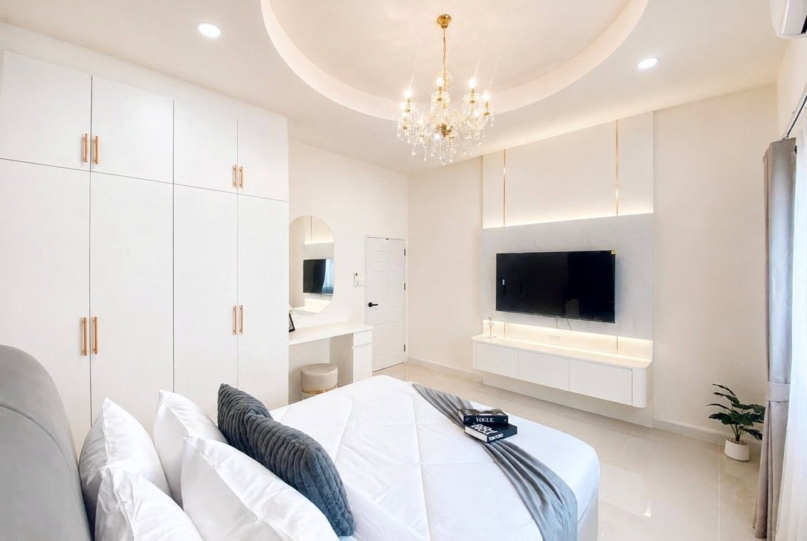 Bright, minimalist bedroom with a chandelier, white cabinetry, and a wall-mounted TV.