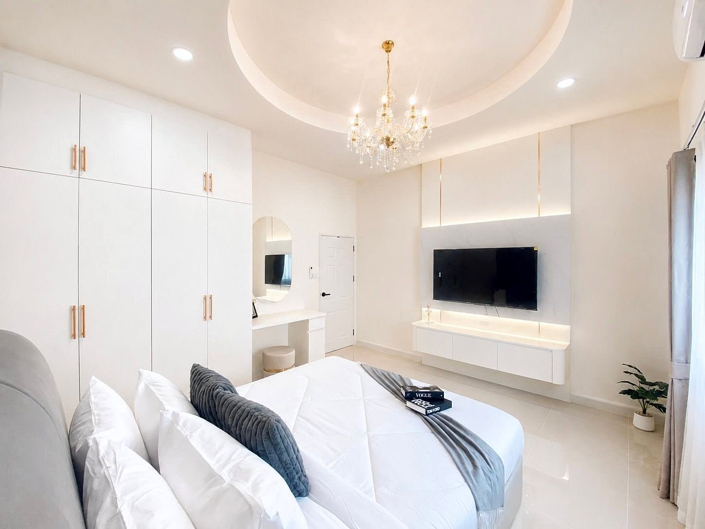 Bright, minimalist bedroom with a chandelier, white cabinetry, and a wall-mounted TV.