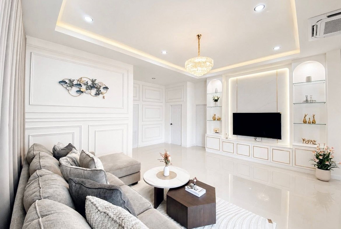 Bright modern living room with a gray sectional sofa facing a wall-mounted TV and white built-in shelving on either side.
