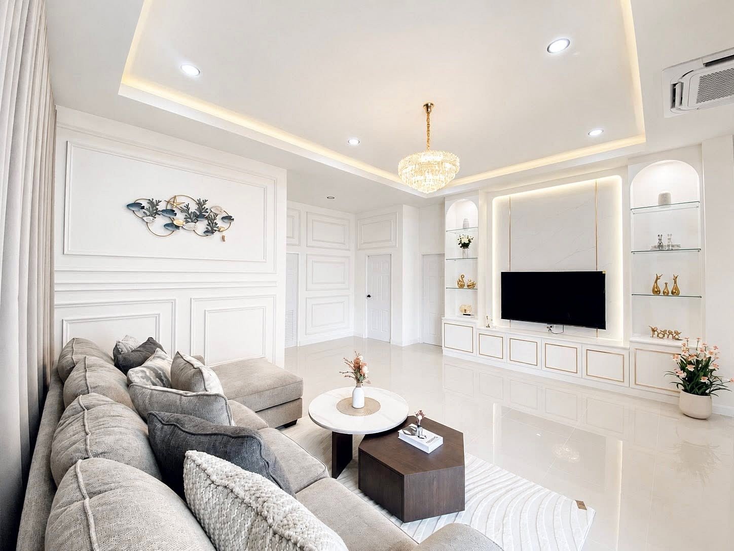 Bright modern living room with a gray sectional sofa facing a wall-mounted TV and white built-in shelving on either side.