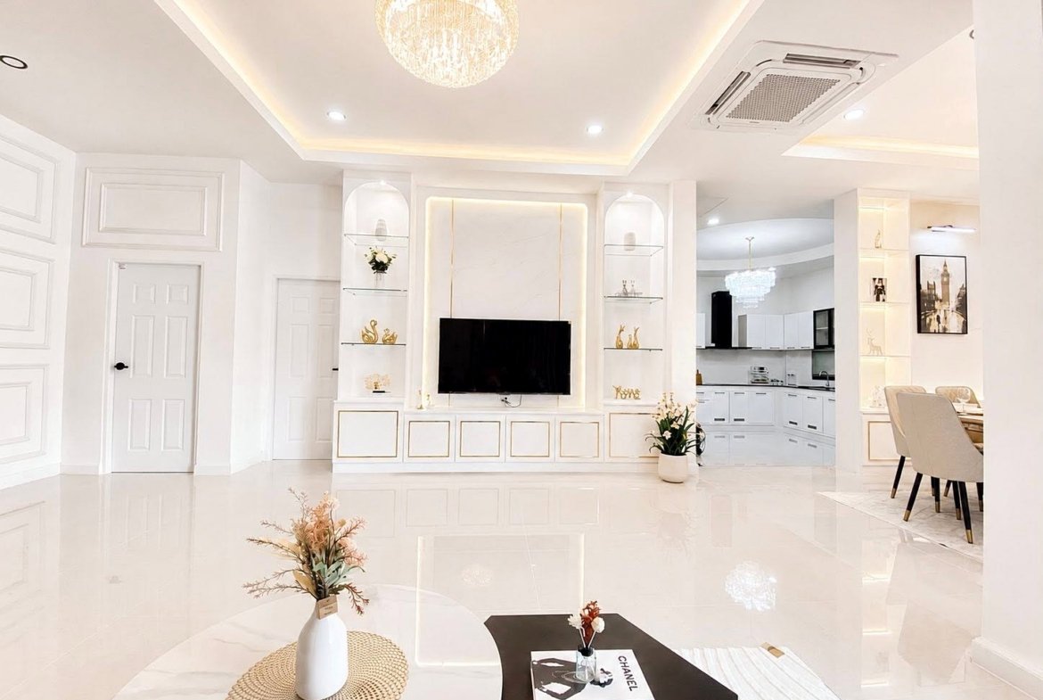 Bright white living room with a wall-mounted TV, glass shelves, and a chandelier above the center.