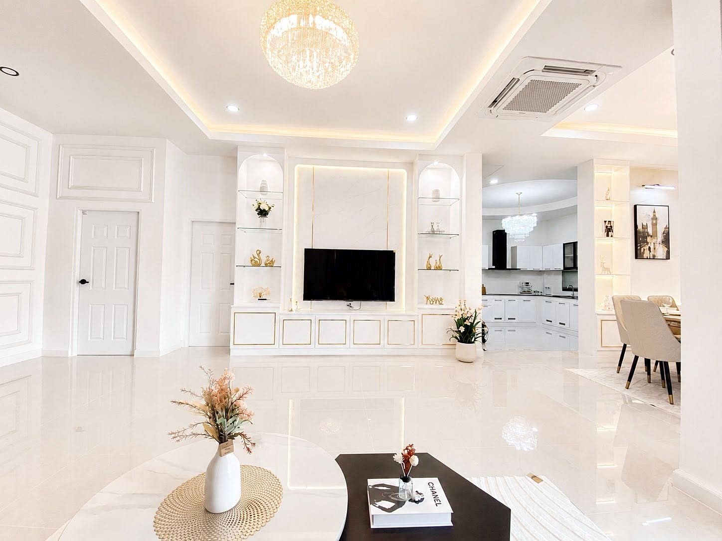 Bright white living room with a wall-mounted TV, glass shelves, and a chandelier above the center.