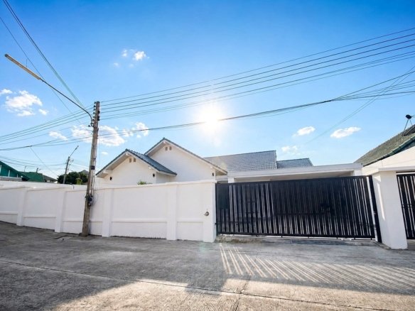 Sunny residential street with white walls a tall black gate and overhead power lines against a blue sky with bright sun