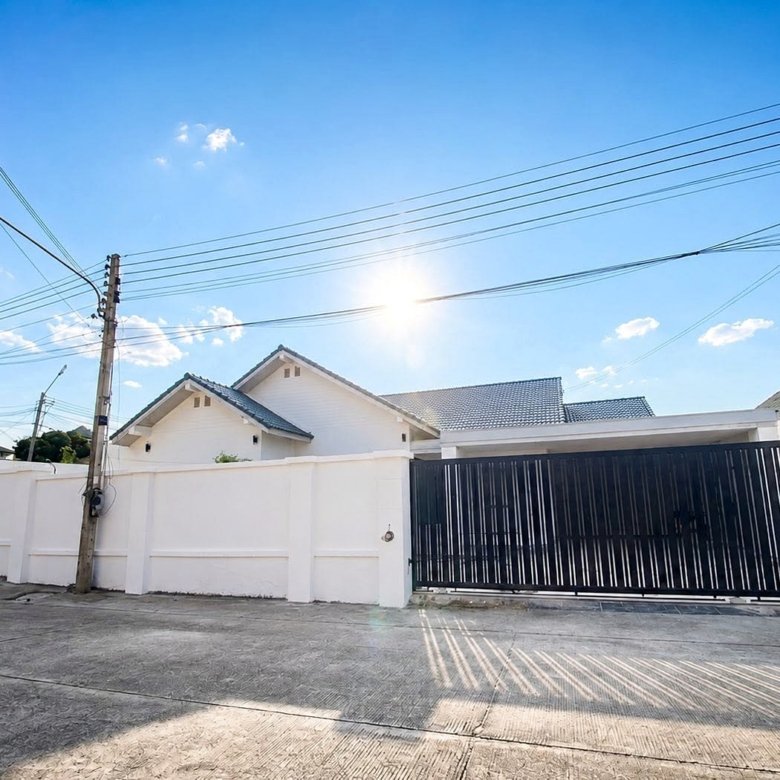 Sunny residential street with white walls a tall black gate and overhead power lines against a blue sky with bright sun