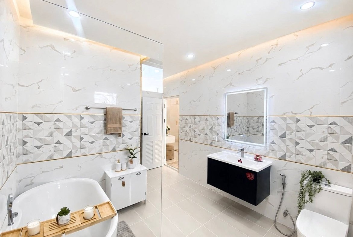 Bright modern bathroom with a freestanding white tub, wooden bath tray with candles, and a wall-mounted sink beneath an illuminated mirror.