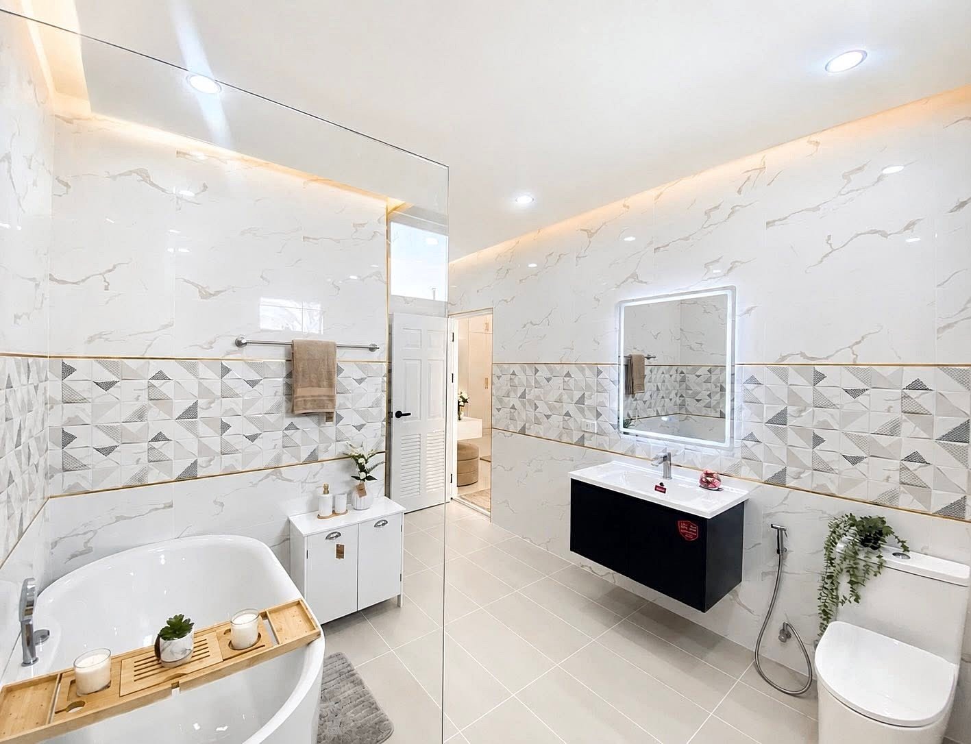 Bright modern bathroom with a freestanding white tub, wooden bath tray with candles, and a wall-mounted sink beneath an illuminated mirror.
