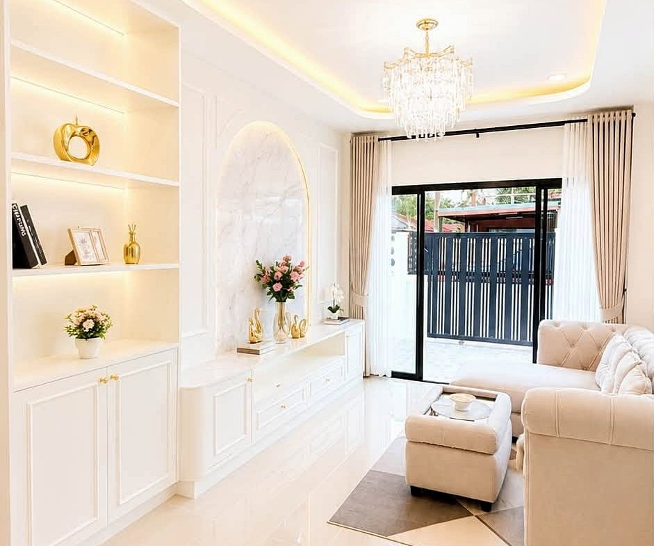 Elegant white living room with built-in shelves, gold decor accents, and a crystal chandelier.