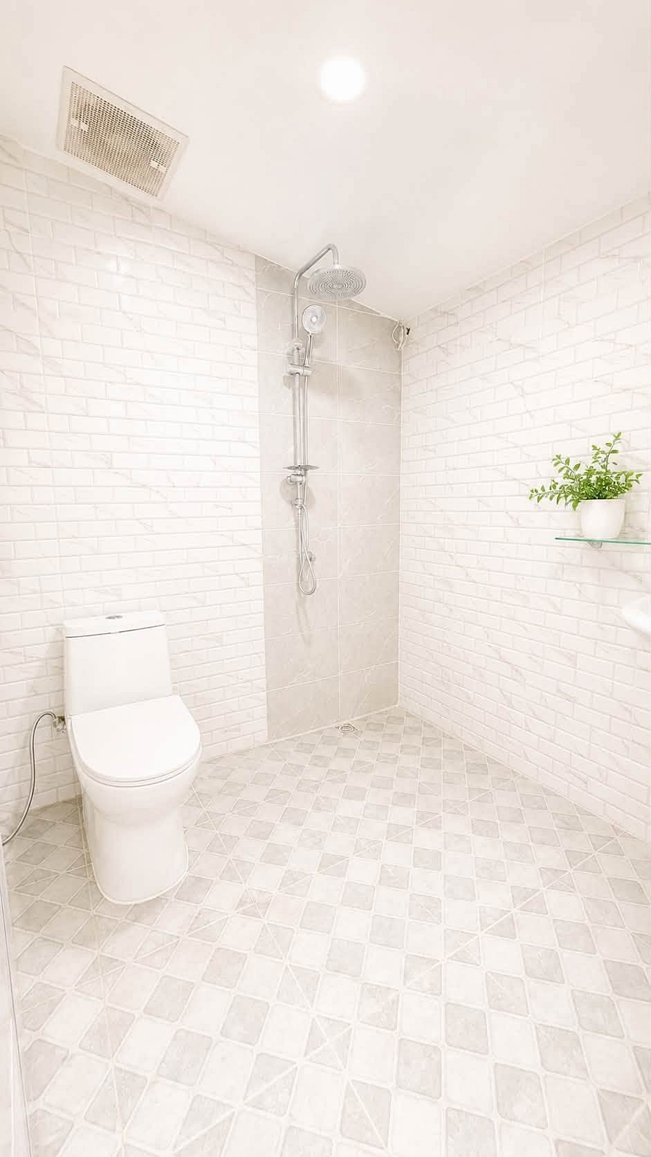 Pattaya_Rungruang_Sale_Dlh579_12 Bright white bathroom with a toilet and a walk-in shower, white brick walls, tiled floor, and a potted plant on a glass shelf.