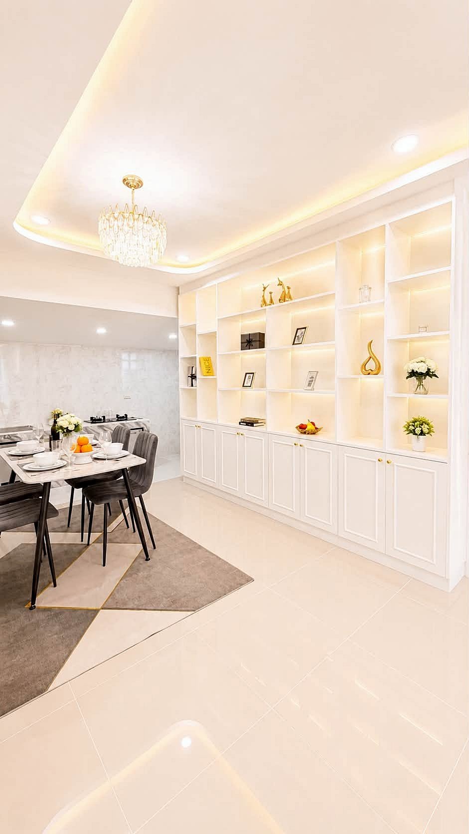 Pattaya_Rungruang_Sale_Dlh579_13 Bright modern dining room with a white built-in shelf wall, crystal chandelier, and a table set for six. Includes a fruit bowl and flowers on the table and soft warm lighting.
