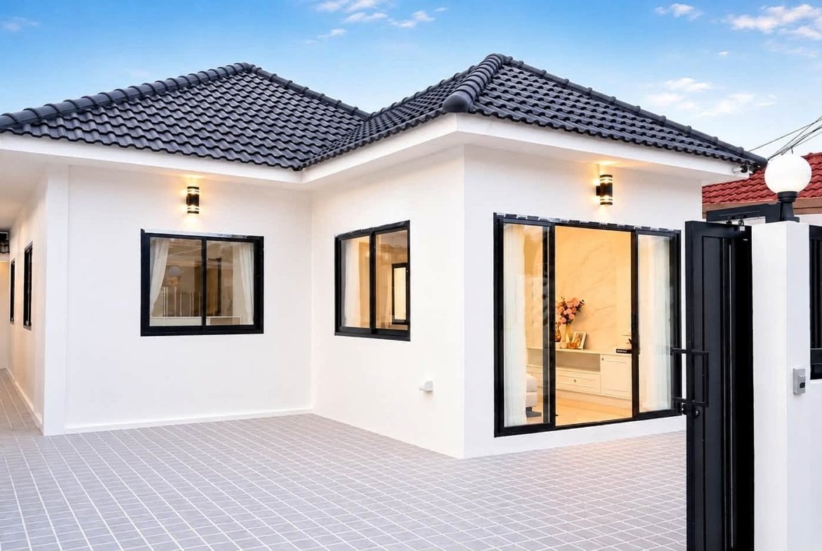 Modern white, single-story home with black-framed windows, gray tiled roof, and an open black gate in a paved courtyard.