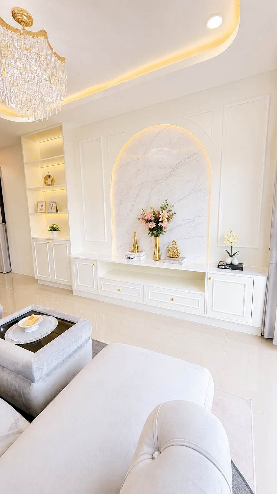 Pattaya_Rungruang_Sale_Dlh579_3 Luxurious white living room with a crystal chandelier and a marble arch niche displaying flowers and decor.