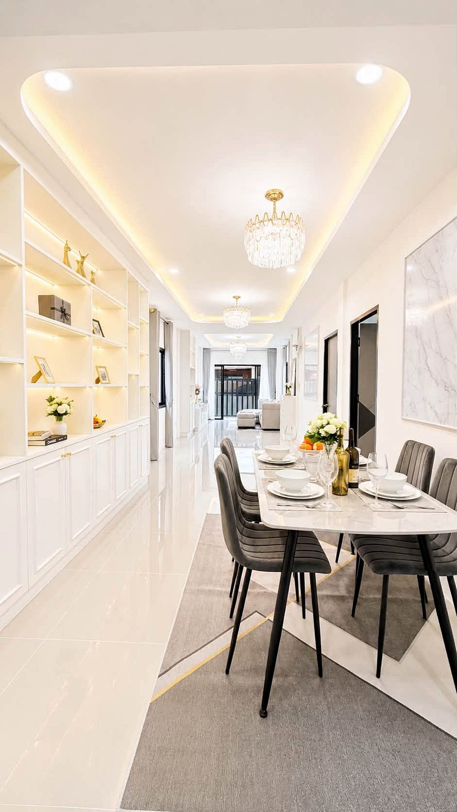 Pattaya_Rungruang_Sale_Dlh579_4 Bright modern dining room with a marble table set for six, white shelves on the left, and crystal chandeliers along a glossy hallway.",