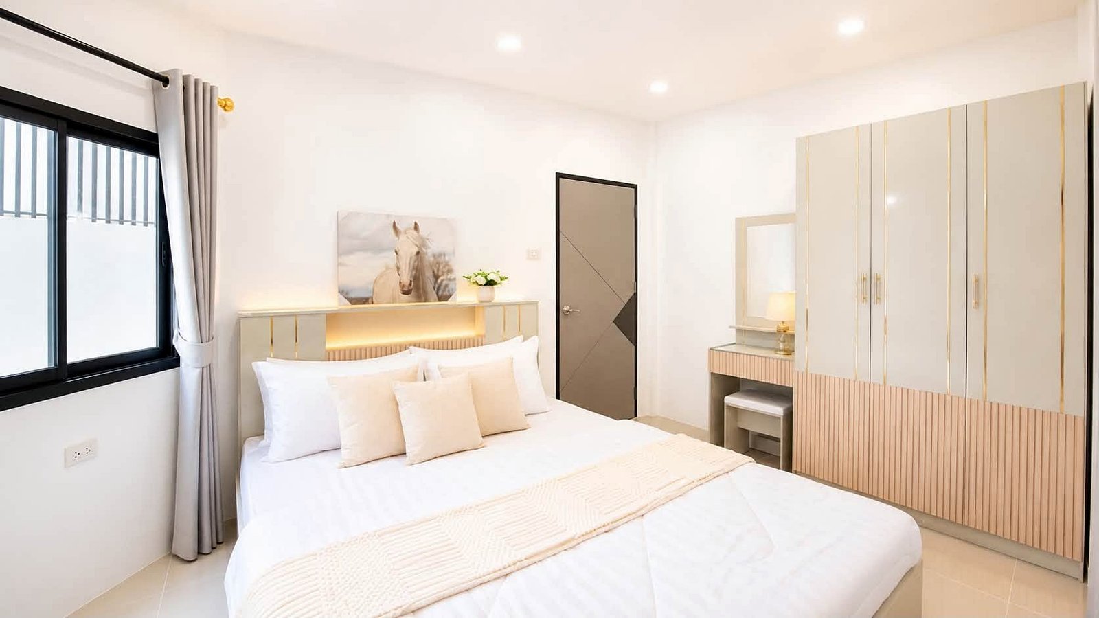 Pattaya_Rungruang_Sale_Dlh579_5 Bright modern bedroom with a large white bed, beige cushions, pale headboard, and a wardrobe along the right side.