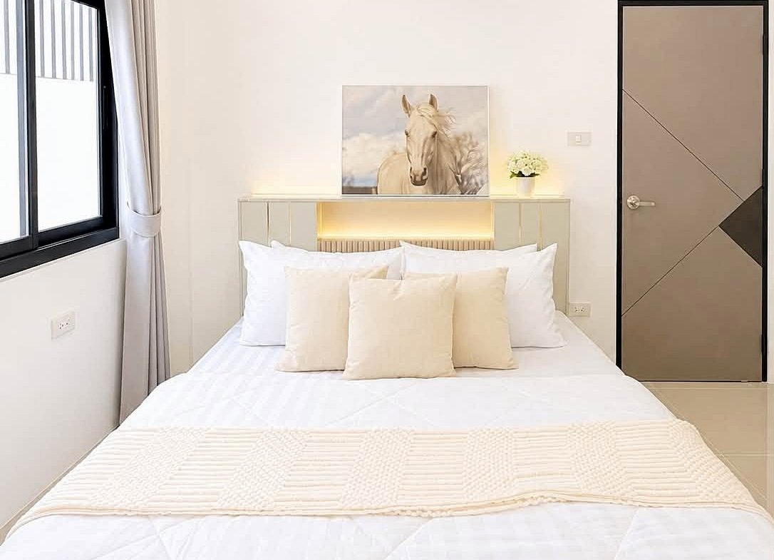 Bright white modern bedroom with a bed, beige throw pillows, and a horse painting above the headboard.