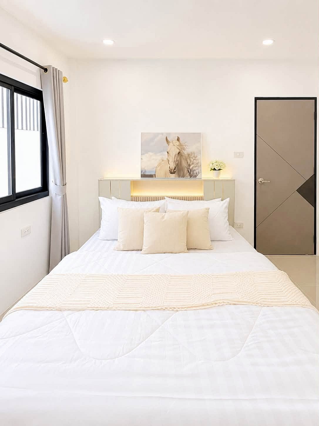 Pattaya_Rungruang_Sale_Dlh579_6 Bright white modern bedroom with a bed, beige throw pillows, and a horse painting above the headboard.