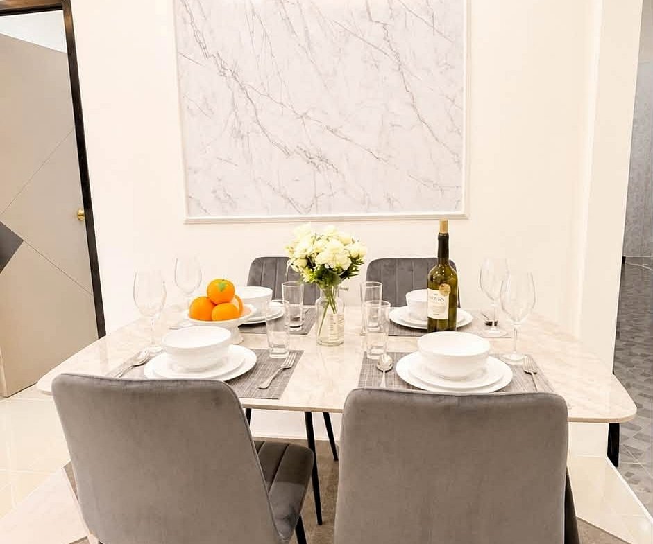 Dining table set for four with white dishes, glasses, and a vase of white flowers; a bottle of wine and oranges on the table.