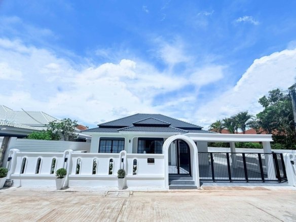 White villa with a decorative arched gate black fence and potted shrubs along a white wall under a blue sky