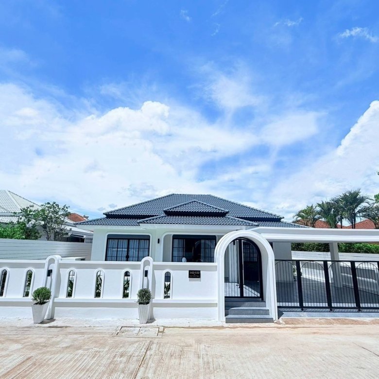 White villa with a decorative arched gate black fence and potted shrubs along a white wall under a blue sky