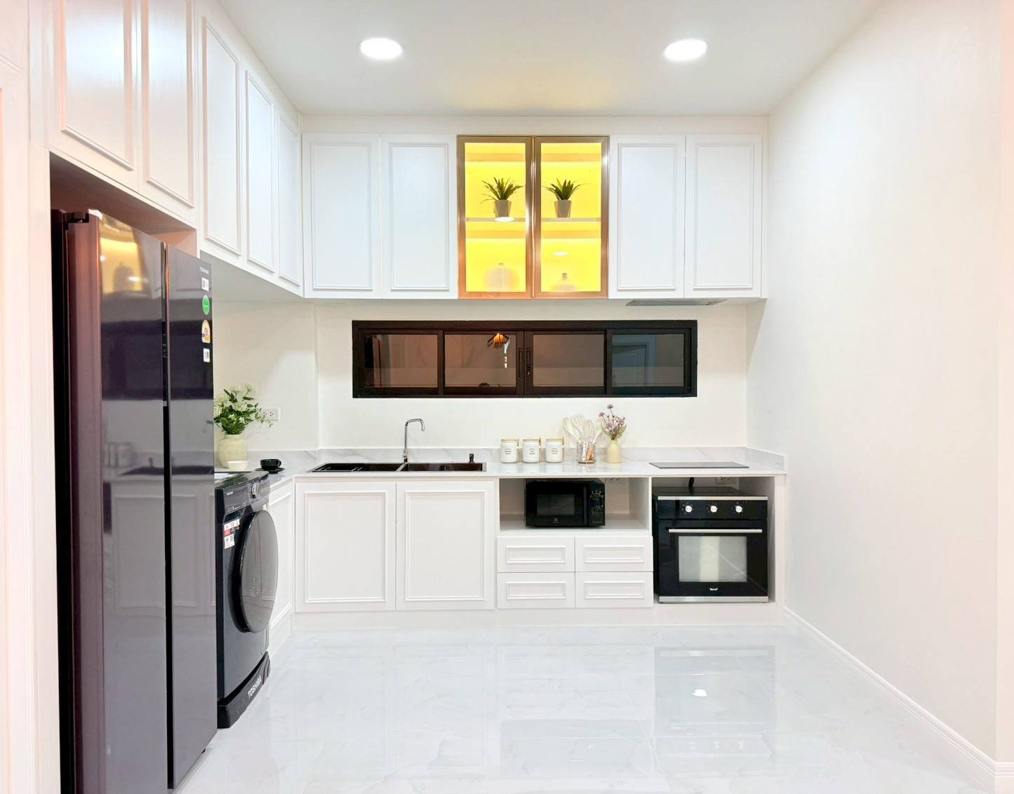 Pattaya_Tropical_2_Village_Dlh535_11 Modern white kitchen with a side-by-side stainless fridge, washing machine, and white cabinets surrounding a marble-like floor.