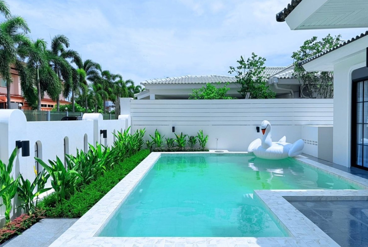 Rectangular backyard pool with turquoise water, white tiled edge, and a large white swan pool float by the steps.