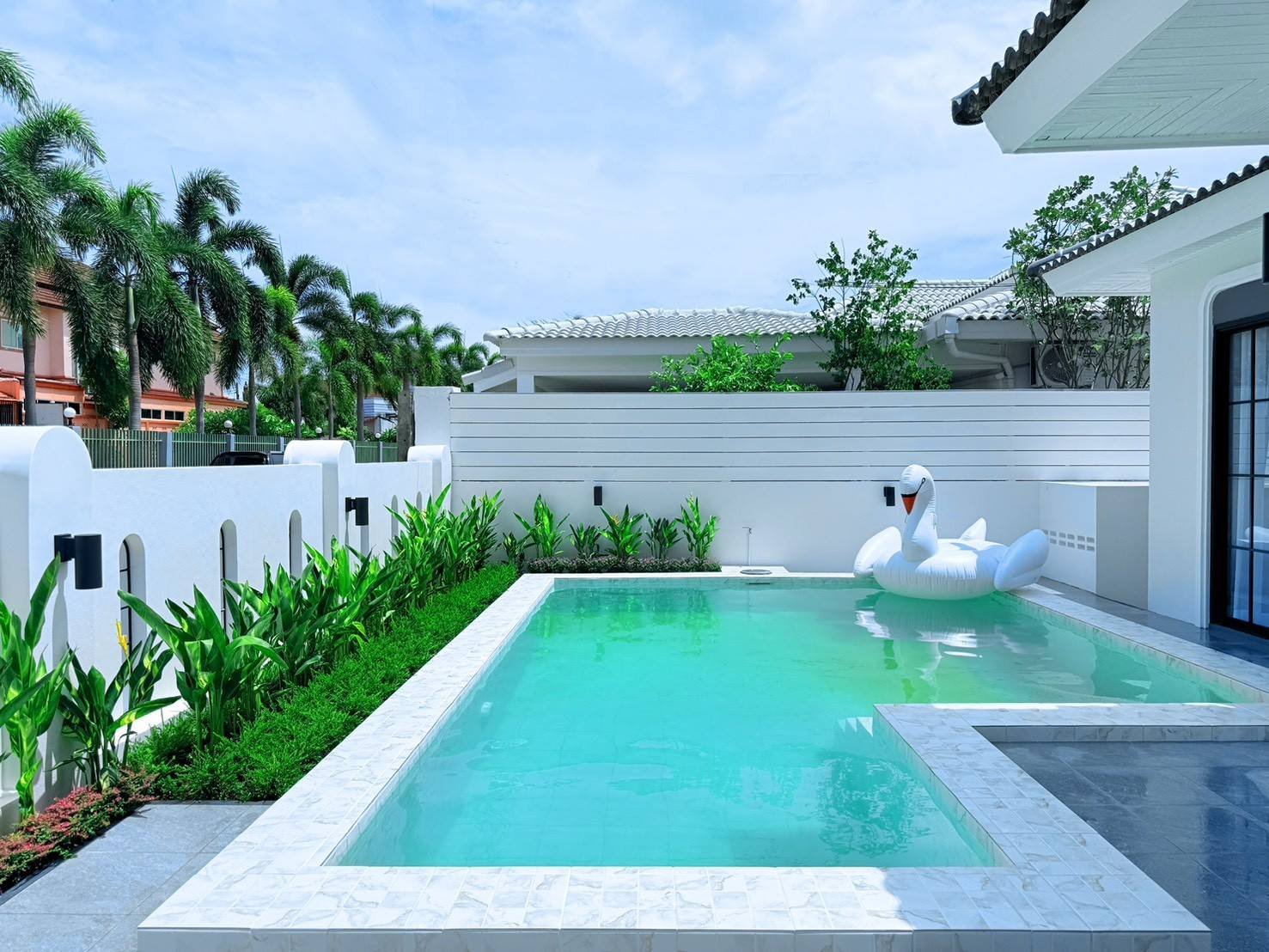 Pattaya_Tropical_2_Village_Dlh535_14 Rectangular backyard pool with turquoise water, white tiled edge, and a large white swan pool float by the steps.