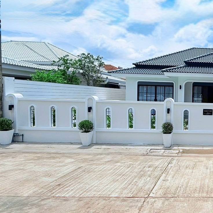 Modern white fence with arched window openings and potted shrubs in front of a contemporary house under a blue sky.