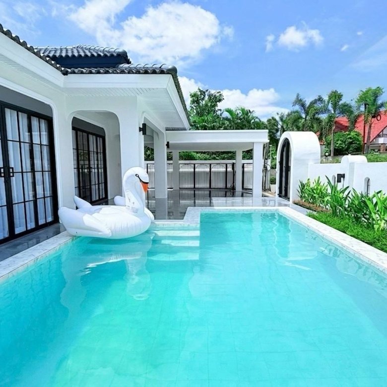 White modern villa with a turquoise rectangular pool and a white swan inflatable near the steps by glass doors