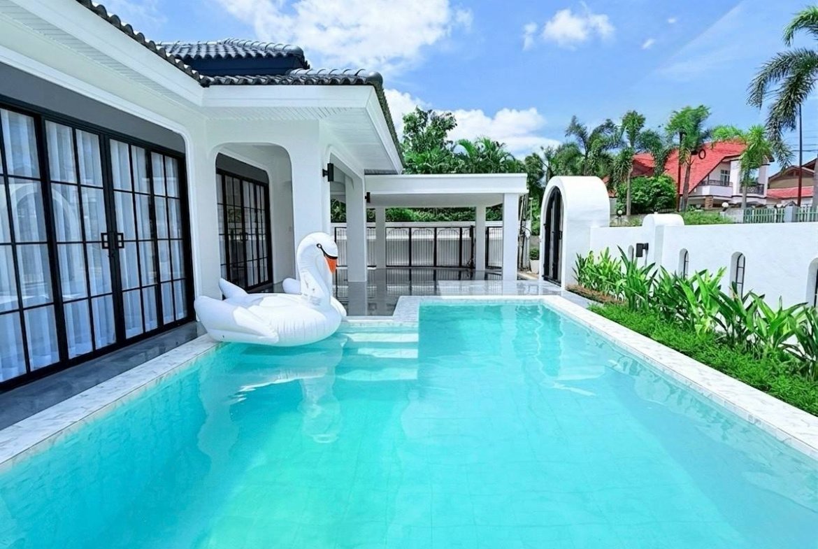 White modern house with a turquoise pool; a white swan float sits near the steps by glass doors.