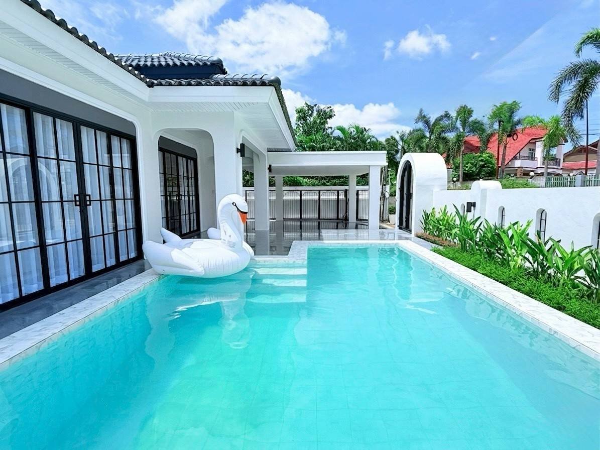 Pattaya_Tropical_2_Village_Dlh535_2 White modern house with a turquoise pool; a white swan float sits near the steps by glass doors.