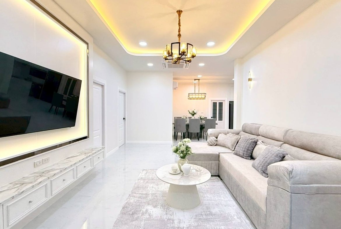 Bright modern living room with a wall-mounted TV, marble floor, and beige sectional sofa. Round marble coffee table in front.