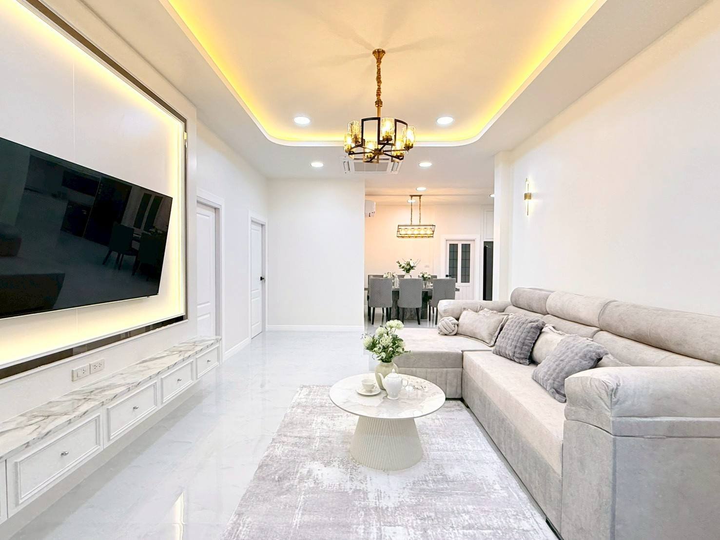 Pattaya_Tropical_2_Village_Dlh535_3 Bright modern living room with a wall-mounted TV, marble floor, and beige sectional sofa. Round marble coffee table in front.